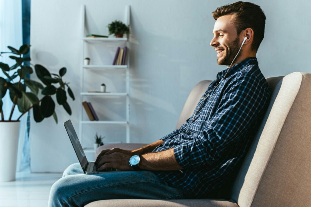 side view of smiling man in earphones taking part in webinar at home